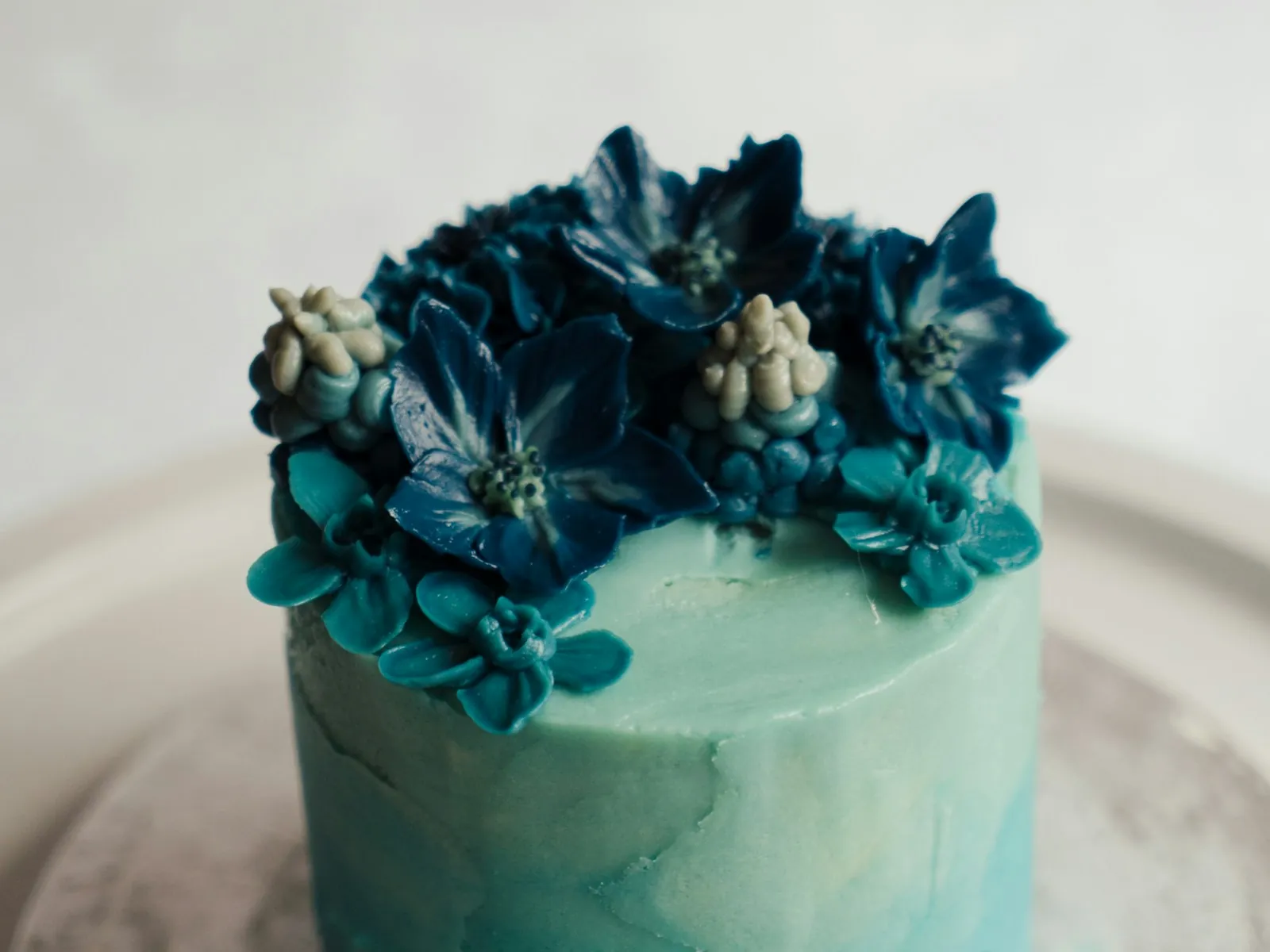 Powder teal floral buttercream cake crowned with deep teal sugar blossoms