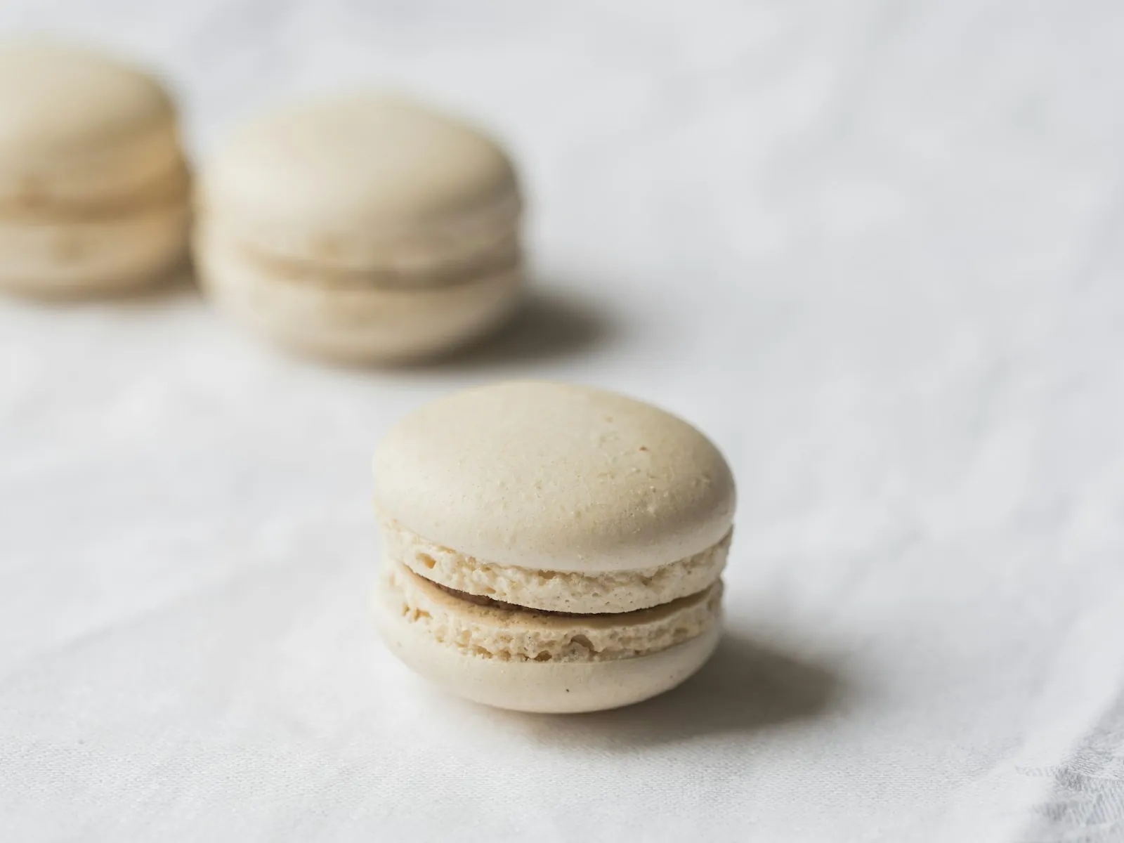 Cream and ivory macaron shells sandwiched with ganache on a marble surface